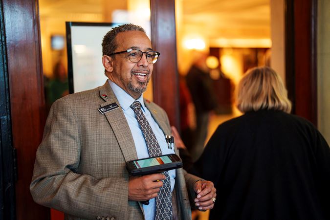house staff supervisor Ed scans an audience member's ticket, looking dapper in a gray suit coat and blue tie