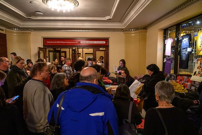a crowd gathers at the Pink Martini merchandise table in the lobby
