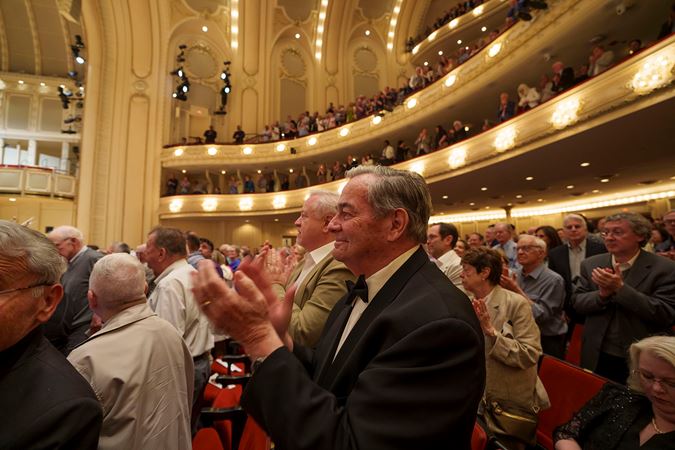 An enthusiastic patron in a black and white suit gives the performers a standing ovation