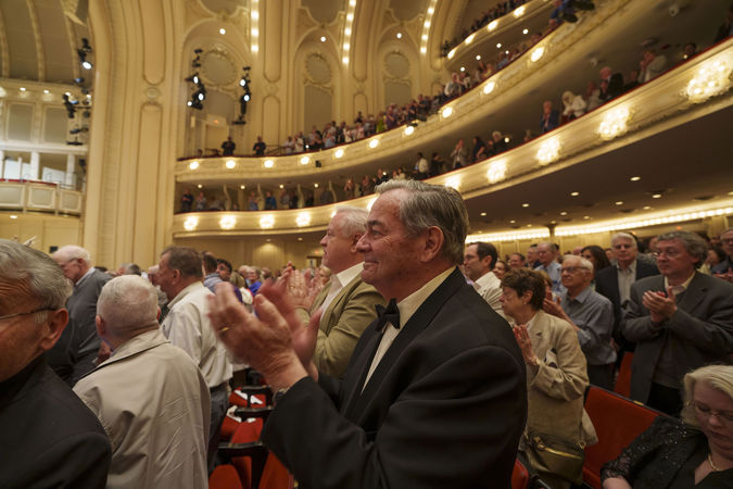 An enthusiastic patron in a black and white suit gives the performers a standing ovation