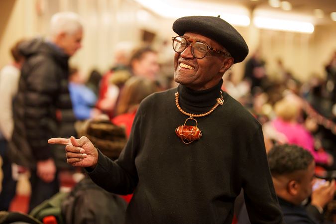 an audience member wearing a hat and colorful necklace takes their seat